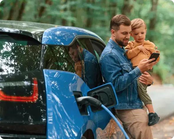 Man holding a child while leaning against and electric vehicle.