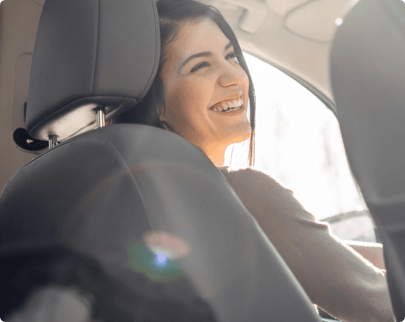 Happy young woman in driver's seat driving after purchasing the right amount of car insurance coverage.
