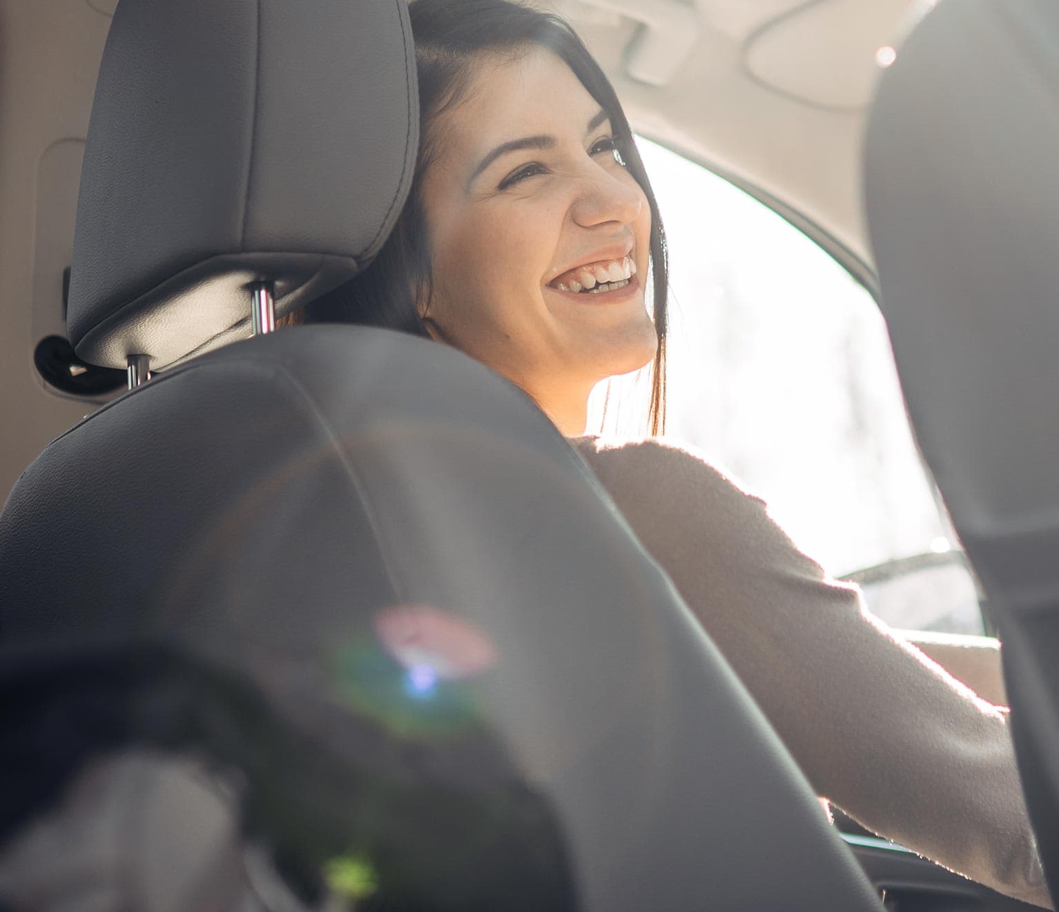 Happy young woman in driver's seat driving after purchasing the right amount of car insurance coverage.