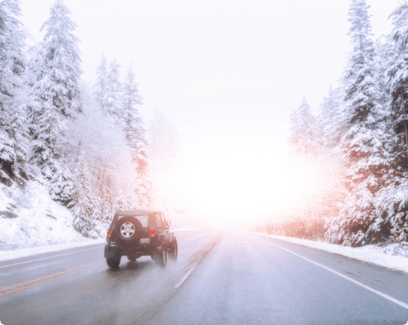 A vehicle driving down an open road surrounded by snow.